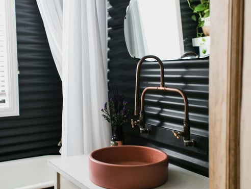 Modern bathroom with round basin and copper tap against dark panel wall