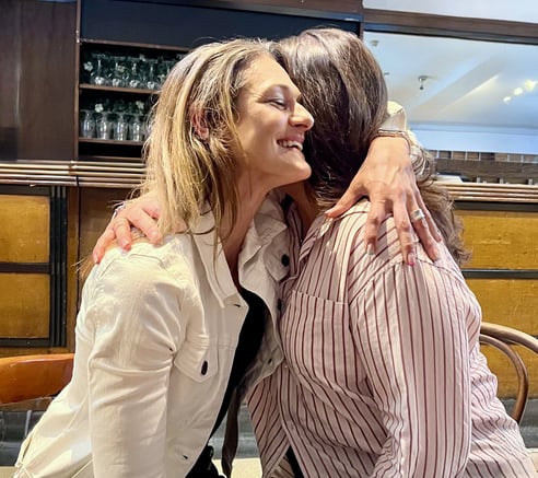 Coach Caroline, hugging a female client in a cafe.