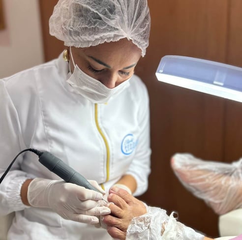 Uma profissional de podologia, vestida com touca descartável, máscara e jaleco branco com detalhes em amarelo