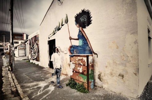 Urban street art photograph by Martin Osner showing a man passing a mural of a woman with headphones and the letters BTS