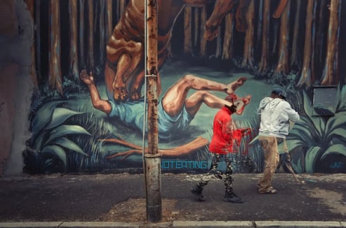 Expressive street photography artwork of men walking past a vivid mural of a tiger attacking a man in Woodstock, Cape Town