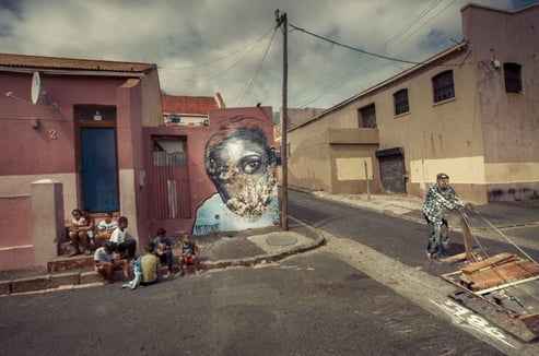Fine art urban street photograph by Martin Osner showing children sitting near a mural and an elderly man pushing a trolley