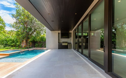 the outside patio of a luxury home with an outdoor grill, pool and deck with sliding glass doors