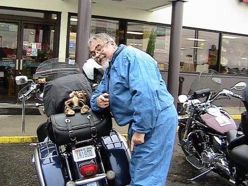 Biker pauses for a picture of a motorcycle and a toy on the back seat.