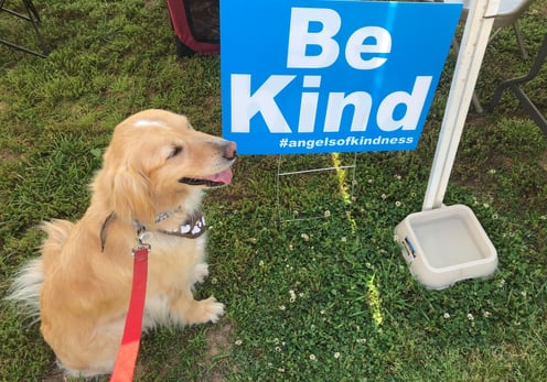 A Therapy Dog sitting next to a "Be Kind" sign