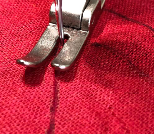 Gros plan sur le pied presseur d'une machine à coudre suivant des lignes sur un tissu