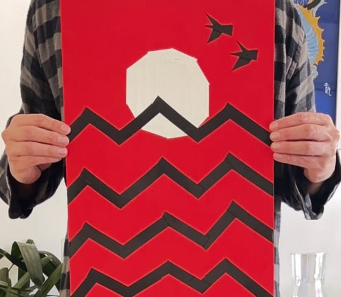 papel vermelho, onde um sol branco está desenhado com fitas, que também fazem o desenho de ondas pretas e duas aves no céu.