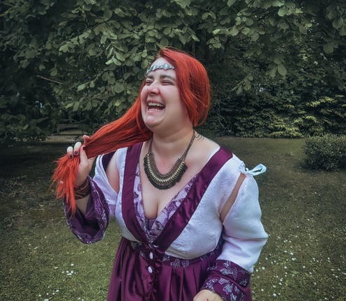 Femme rousse riante et joyeuse dans une robe violette et blanche dans un fond verdoyant