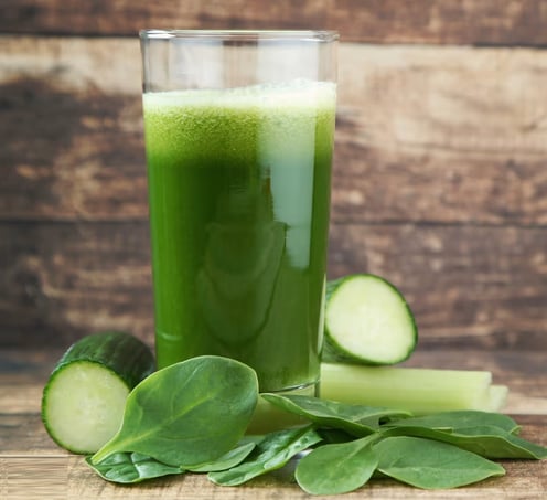 a glass of green juice with a slice of cucumber on the side