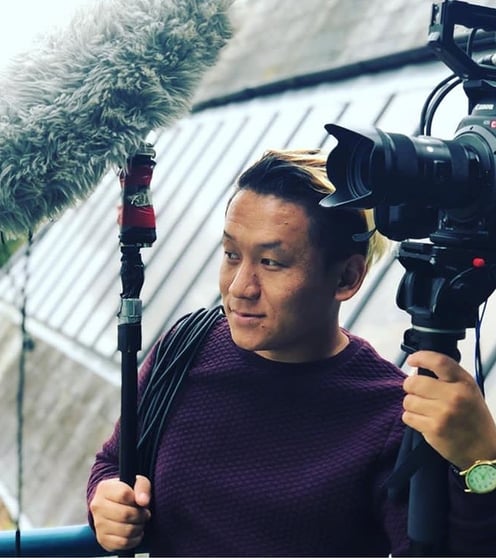 a man in a purple sweater holding a microphone and a video camera