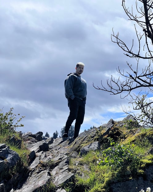 a man standing on a rocky cliff with a tree in the background
