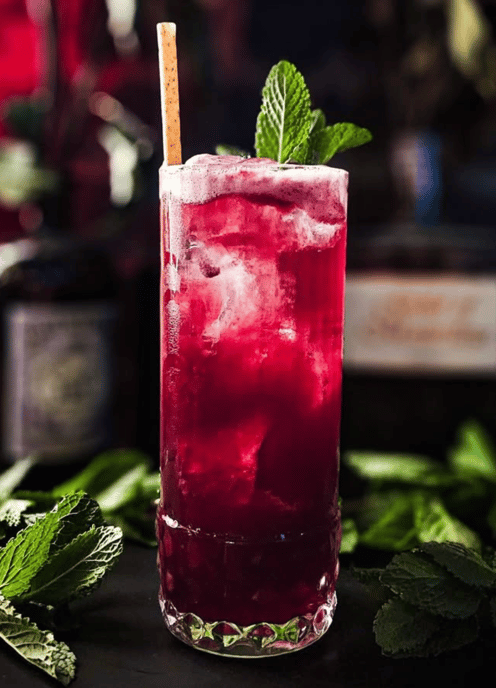 a glass of alcohol with a strawberries and mint leaves