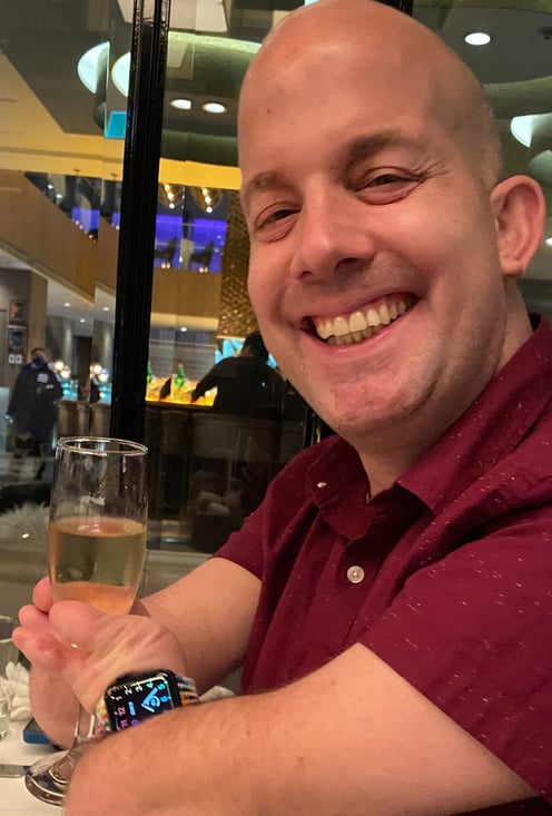 Yoav Rokach Penn wearing a red dress shirt, in a restaurant holding a Champaign glass.