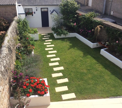 Jardin paysager avec gazon, massifs fleuris et pas japonais menant à une entrée de maison