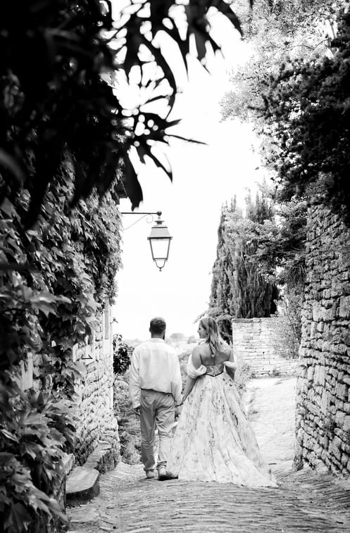 Black and white photo of couple walking hand in hand — cobblestone alley in a Provençal village