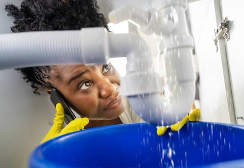 woman on the phone staring at her leaking pipe