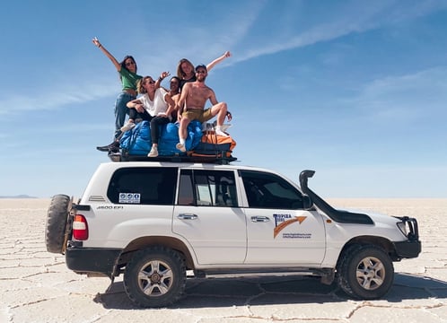 Group of friends sitting on the roof of a 4x4 in the Uyuni Salt Flat.