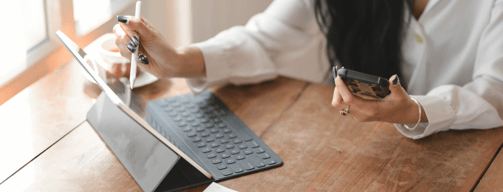 a woman sitting at a table with a mobile phone and a tablet reviewing company information