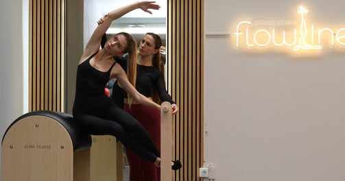Instrutora de Pilates ajudando uma aluna a fazer um alongamento lateral no ladder barreldel