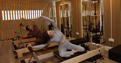 Three people performing a side stretch on reformers in a Pilates studio with wooden accents 