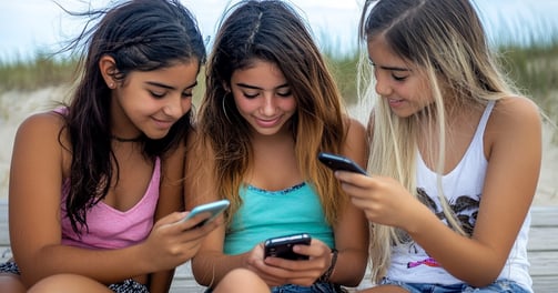 Fotografía de 3 adolescentes viendo sus celulares en la playa 