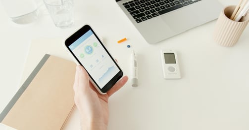 Person holding a Glucose monitor reader at a computer desk