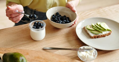 Person eating blueberries, yoghurt, avocado on toast