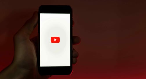 Hand holding a phone displaying the YouTube logo on a dark background