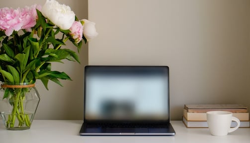 a black laptop on a desk with flowers in a vase