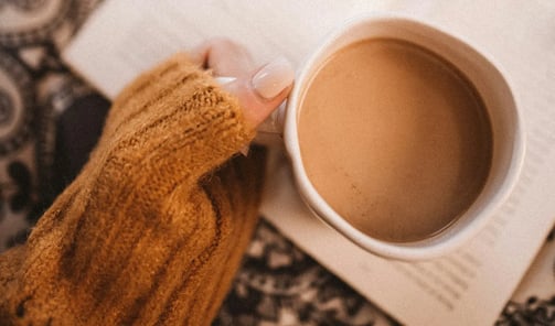 Main de femme tenant une tasse de café sur un livre, symbole d’ancrage doux et d’exploration intérie