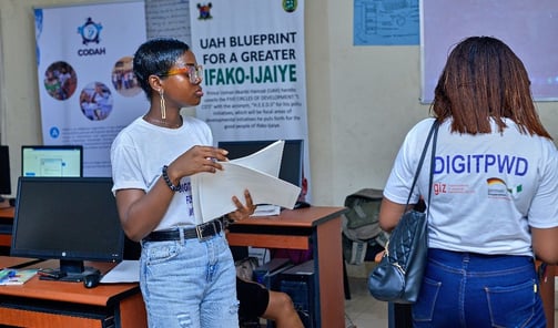 2 girls standing on opposite sides, with one having an inscription on the back of her shirt "DIGITPWD"