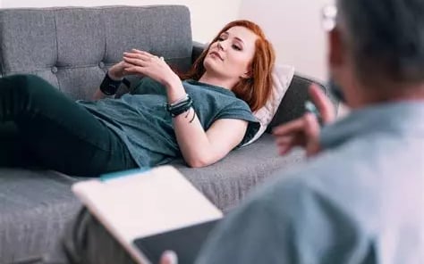 femme allongée sur un canapé en état d'hypnose et son thérapeute de dos qui la guide