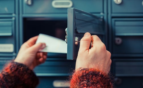 a person holding a piece of mail in front of a lockable post box