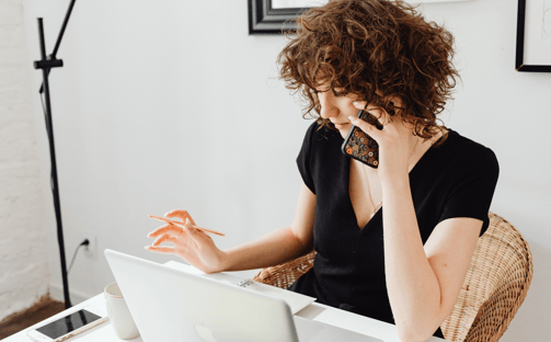 a woman sitting at a table with a laptop and a mobile phone