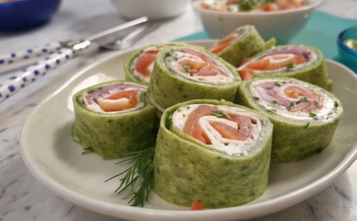 a plate of food that includes salmon, cucumber, cream cheese, pinwheels