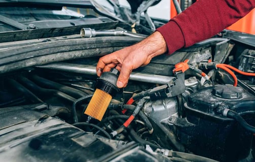 a man is holding a filter in his hand while he is working on a car