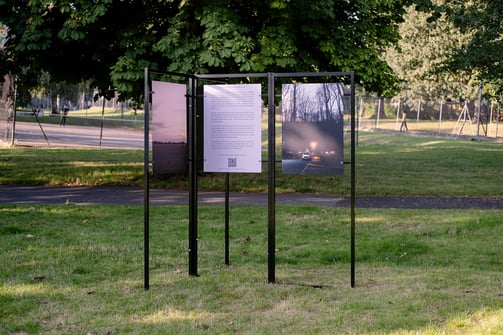 three photographs exhibited on black metal stands in a park