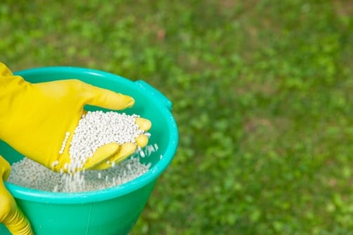 a person with a yellow glove sifting through fertilizer pellets in a yellow bucket