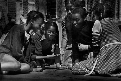 a group of young Black girls sitting on the ground playing jacks