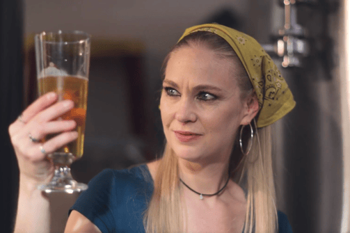 a woman in a blue shirt and a yellow headband holding a glass of beer