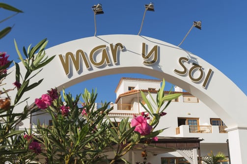 entrada del hotel mar y sol con arco blanco y escrita color oro