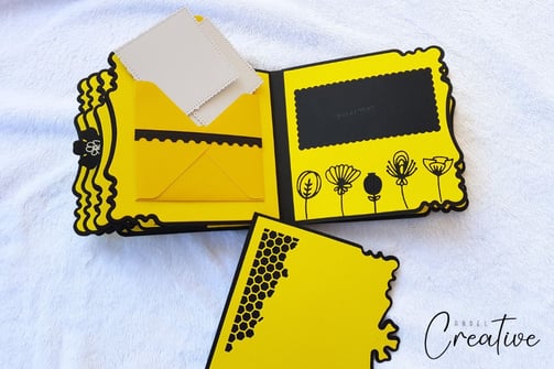 Yellow handmade scrapbook album with black floral and honeycomb designs. Open envelope holds white c