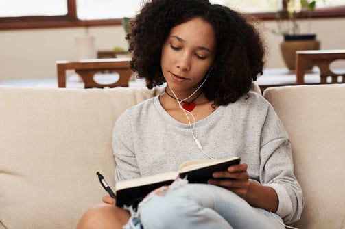 a woman sitting on a couch with headphones journaling in a notebook on