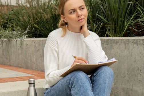 a woman sitting on a concrete step reflecting on herself writing her accomplishments