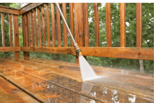 Power washing a wooden deck to remove dirt and buildup during an exterior cleaning service