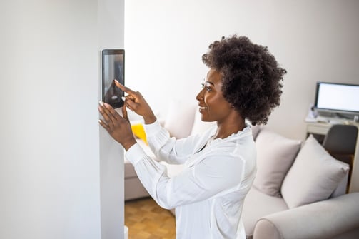 black woman adjusting smart home via tablet on the wall