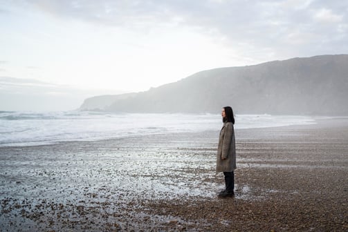 a woman standing on a beach with a mountain in the background
