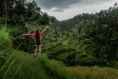 a woman standing on a hill with palm trees in the background