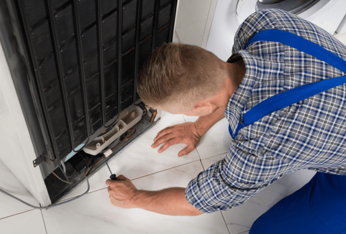 a man in a blue shirt is fixing a dishwasher