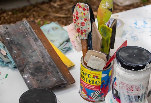 Printmaking materials resting on a table, including spatulas, ink, and a squeegee.